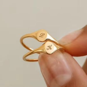 Gold ring with engraved initials held by a hand against a neutral background