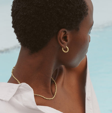 Person wearing a gold necklace and hoop earring by a pool
